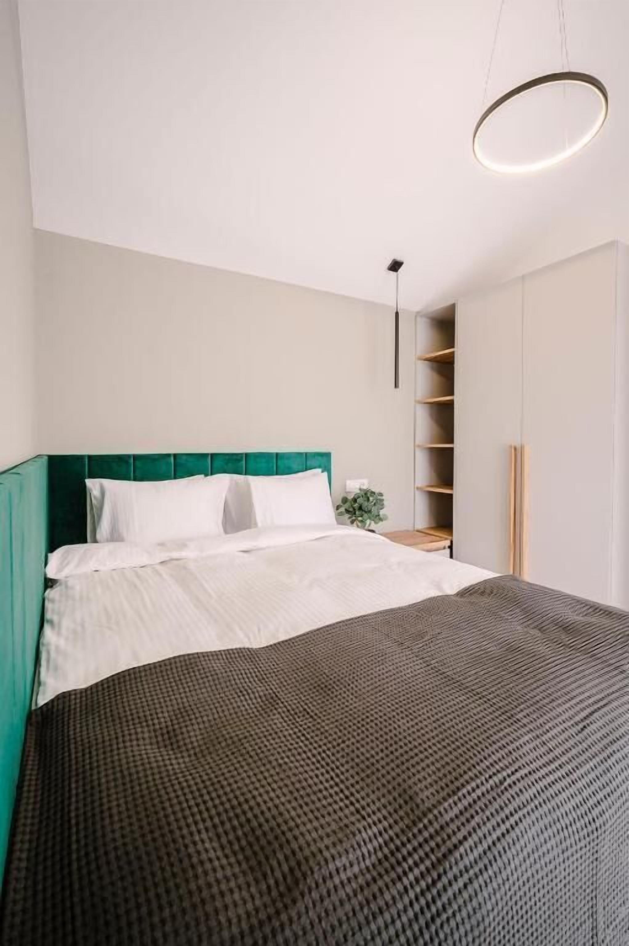 A bedroom with a bed, a green headboard, a bedside table with a plant, and a built-in shelving unit.