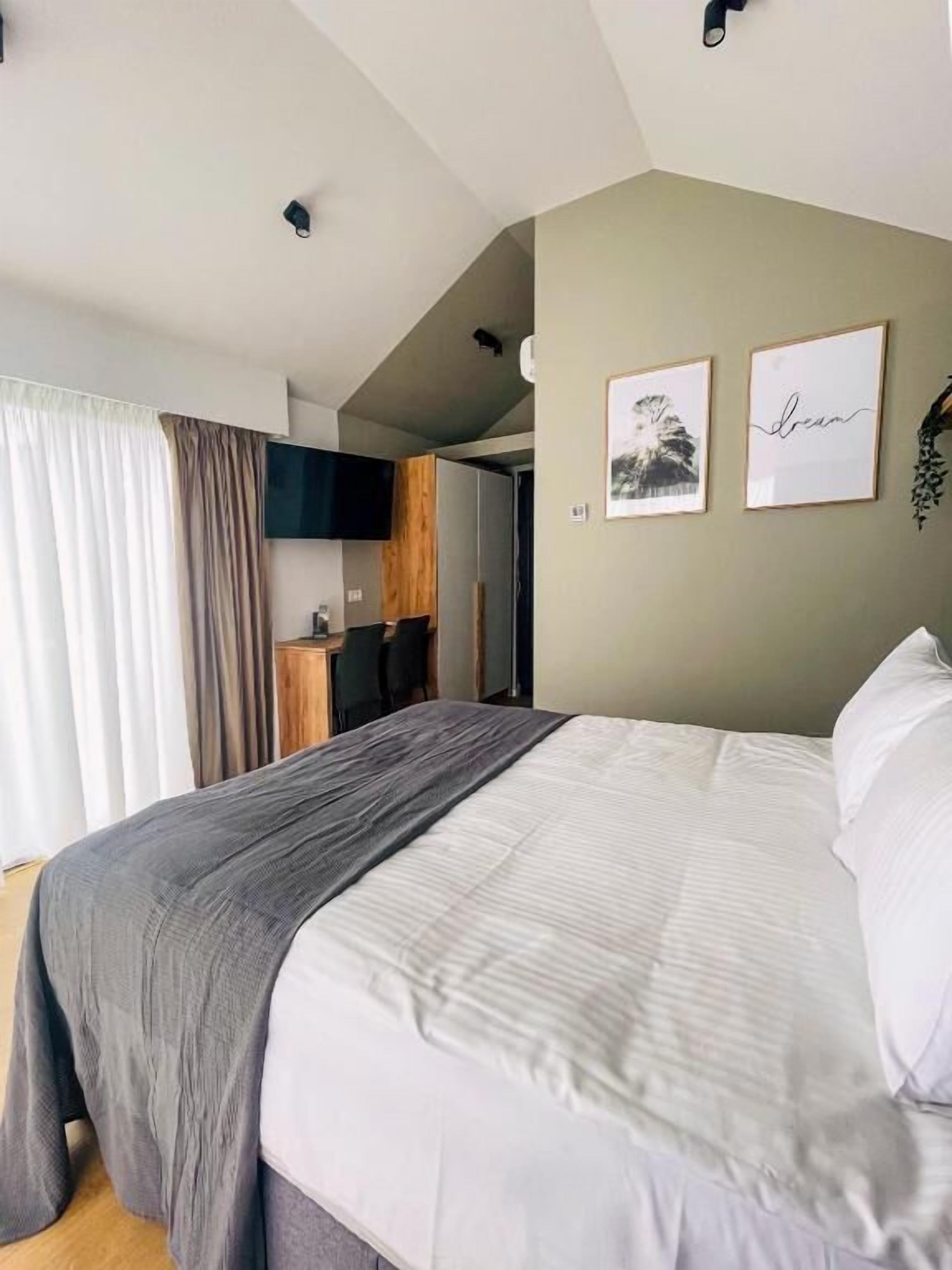 Quarto moderno com uma cama grande, televisão na parede e uma cozinha compacta ao fundo.