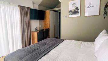 Quarto moderno com uma cama grande, televisão na parede e uma cozinha compacta ao fundo.