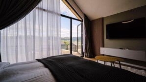 Habitació d'hotel moderna amb un llit gran, una televisió de pantalla plana penjada a la paret i un balcó amb vista a les muntanyes.
