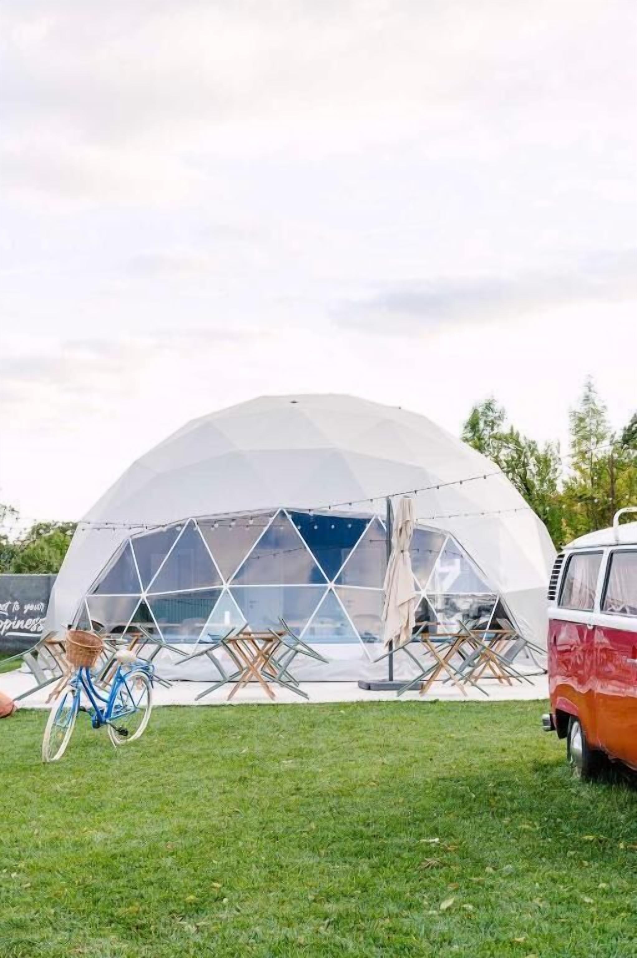Una estructura de domo geodésico con techo transparente, rodeada de mobiliario exterior y una bicicleta.