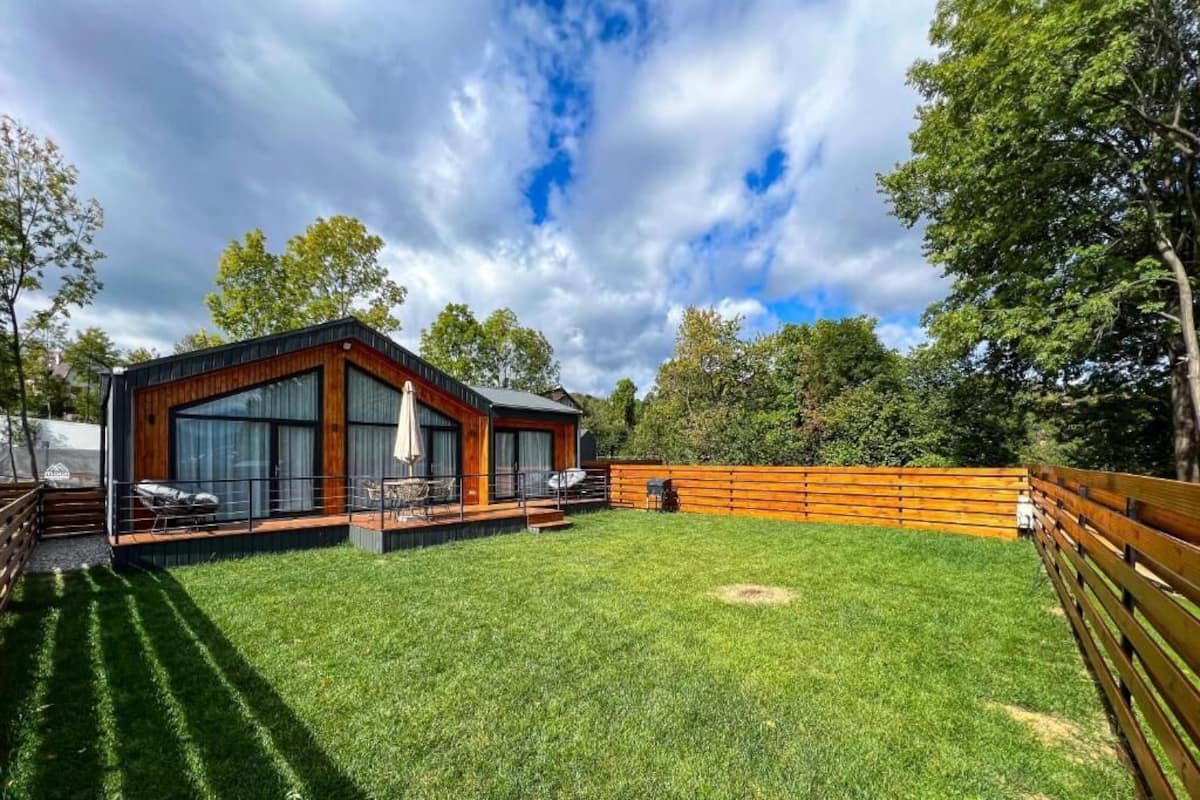 A modern house with a deck, surrounded by a wooden fence and a well-maintained lawn.