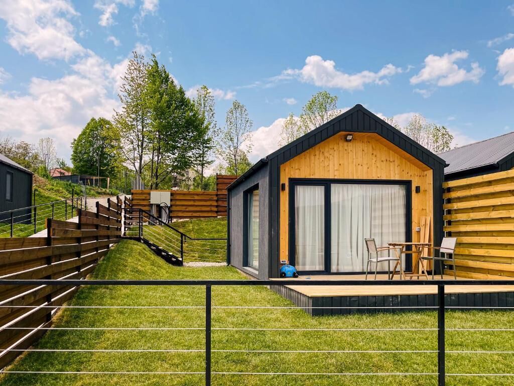 A modern cabin with a wooden exterior, a large garage door, and a small patio area with outdoor seating.