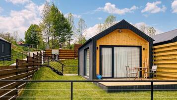 Una cabana moderna amb façana de fusta, una porta garatge gran i una petita zona de terrassa amb mobiliari exterior.
