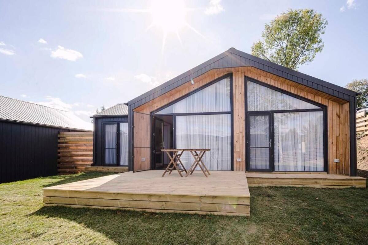A modern house with a wooden exterior, large windows, and a wooden deck with a table.