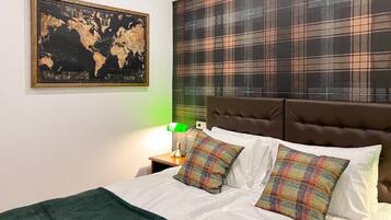 Una cama bien hecha con almohadones escoceses, un mapa del mundo en la pared y un cabecero a cuadros.