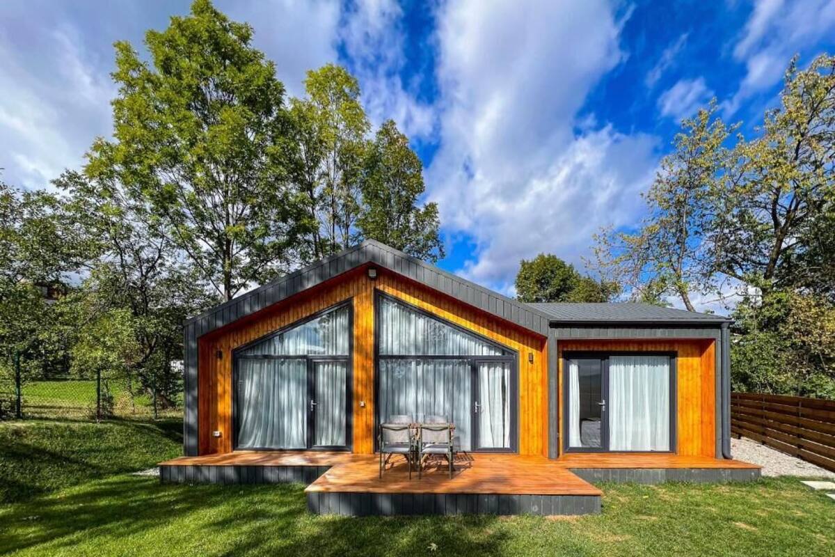 A modern house with a wooden deck, large windows, and a fenced yard.
