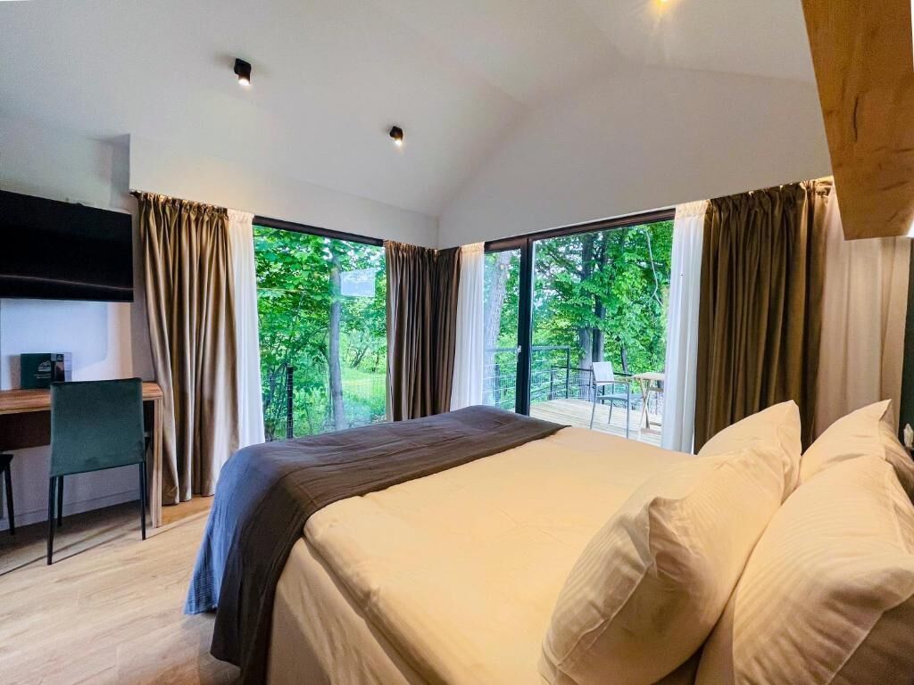 Een moderne slaapkamer met een groot bed, een bureau en uitzicht op groen door de ramen.