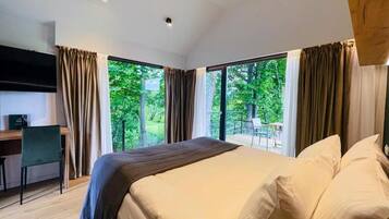 Een moderne slaapkamer met een groot bed, een bureau en uitzicht op groen door de ramen.