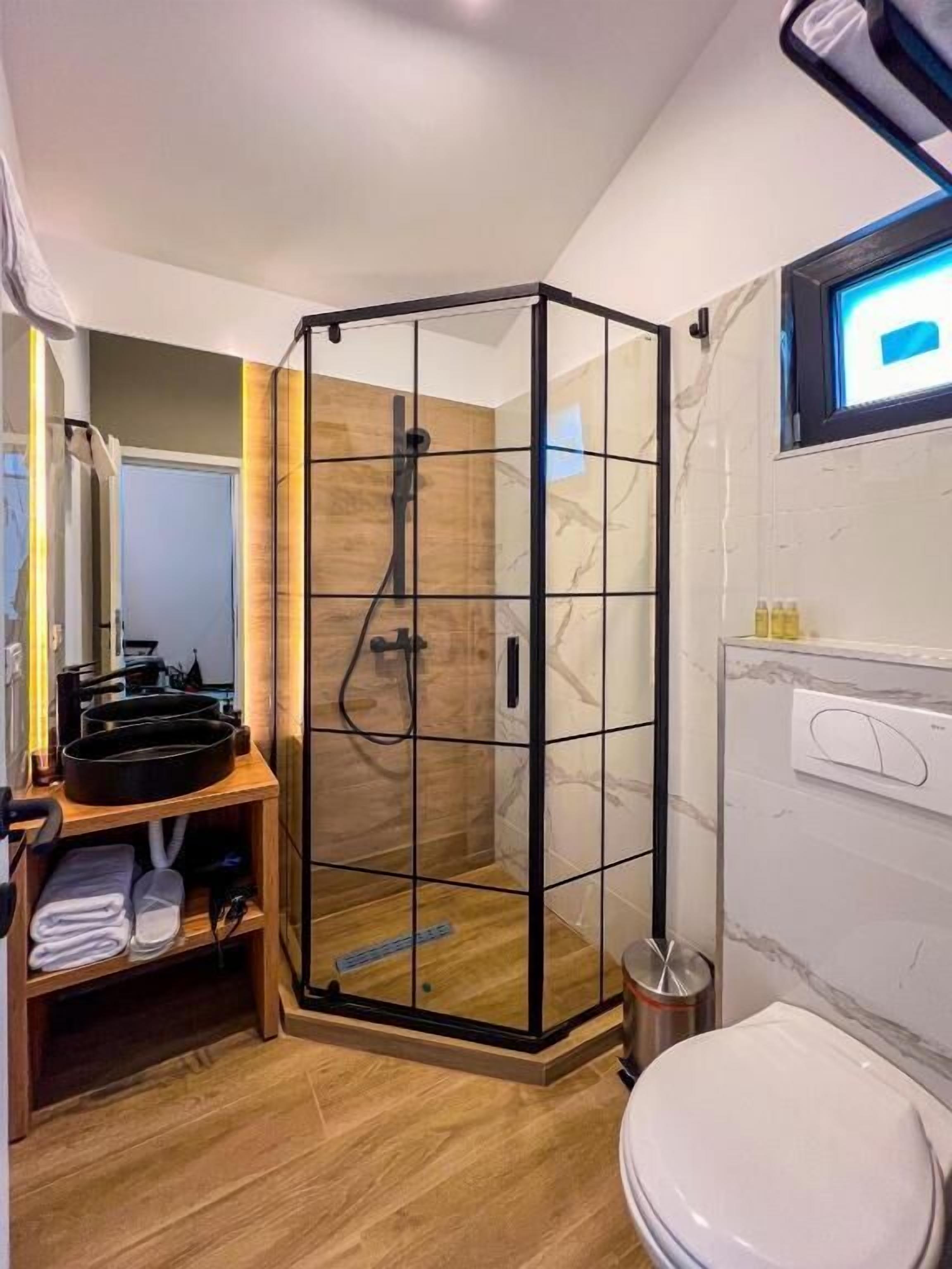 A modern bathroom with a glass-enclosed shower, a wooden vanity, and a white toilet.