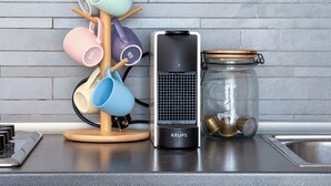 A kitchen counter with a coffee maker, a mug rack, and a jar with brass lids.