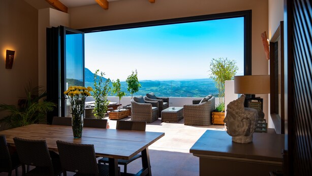 A modern outdoor seating area with wicker furniture, a wooden table, and a vase of yellow flowers.