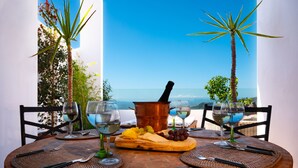 A table set with a cheese board, grapes, and wine glasses, overlooking a beach.