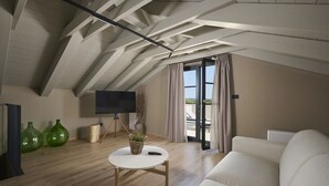 A modern loft bedroom with a sloped ceiling, a large window with curtains, a flat-screen TV on a tripod, a round coffee table with a plant, and a white sofa. - Villa Madora in Porec (Porec)