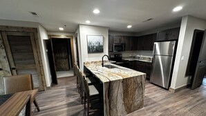 A modern kitchen with a marble island, stainless steel appliances, and a wooden dining area.