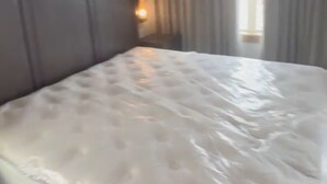 A hotel room with a large bed, a painting on the wall, and a window with curtains.