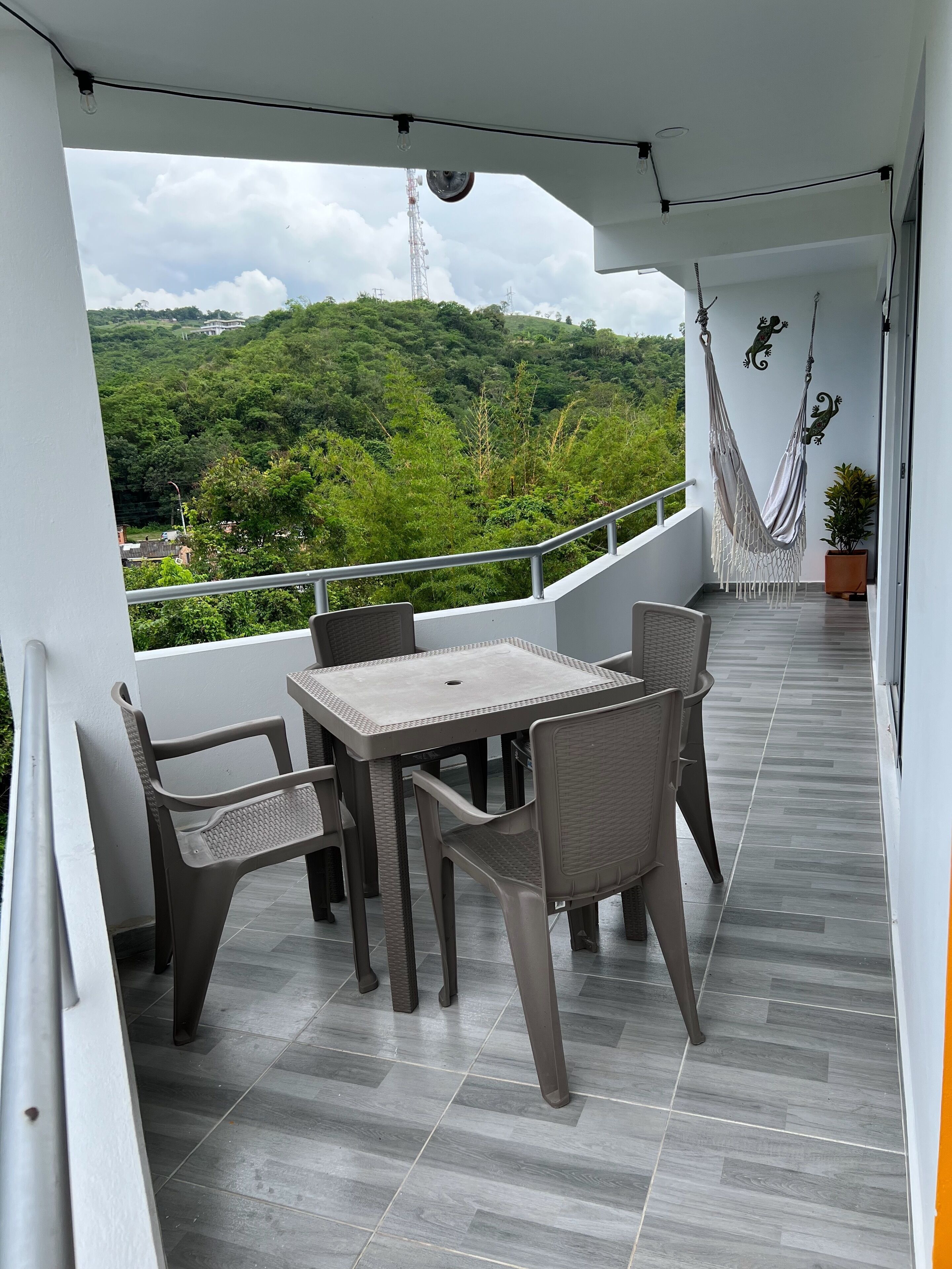 Un balcone con tavolo e sedie, un'amaca e vista su un paesaggio verde.