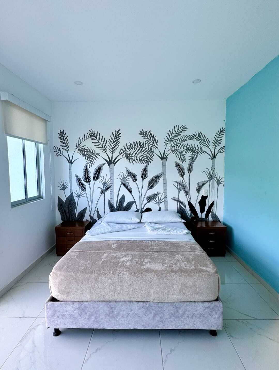 Une chambre à coucher avec un lit, une fenêtre et un mur décoré d’une fresque représentant des plantes.