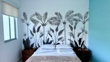 Une chambre à coucher avec un lit, une fenêtre et un mur décoré d’une fresque représentant des plantes.