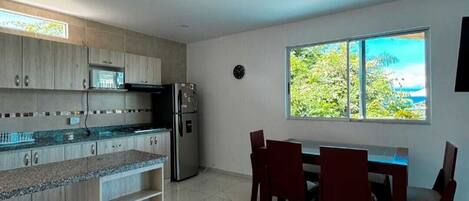 Una cocina moderna con encimeras de granito, un comedor con mesa y sillas, y un amplio ventanal con vistas a zonas verdes.