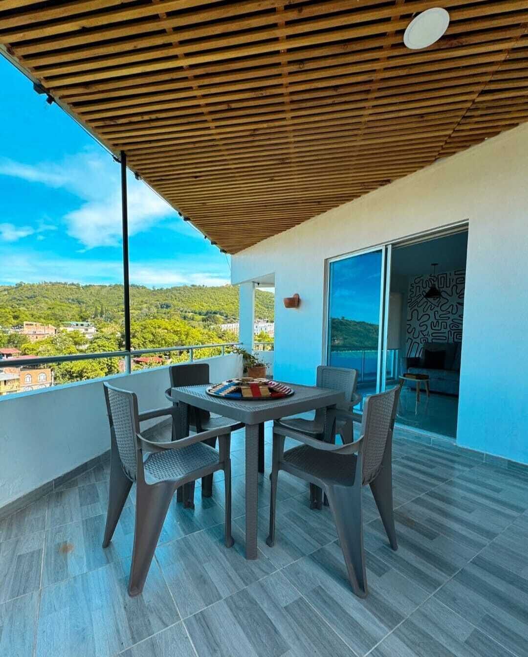 A balcony with a wooden ceiling, a table with chairs, and a view of a green landscape.