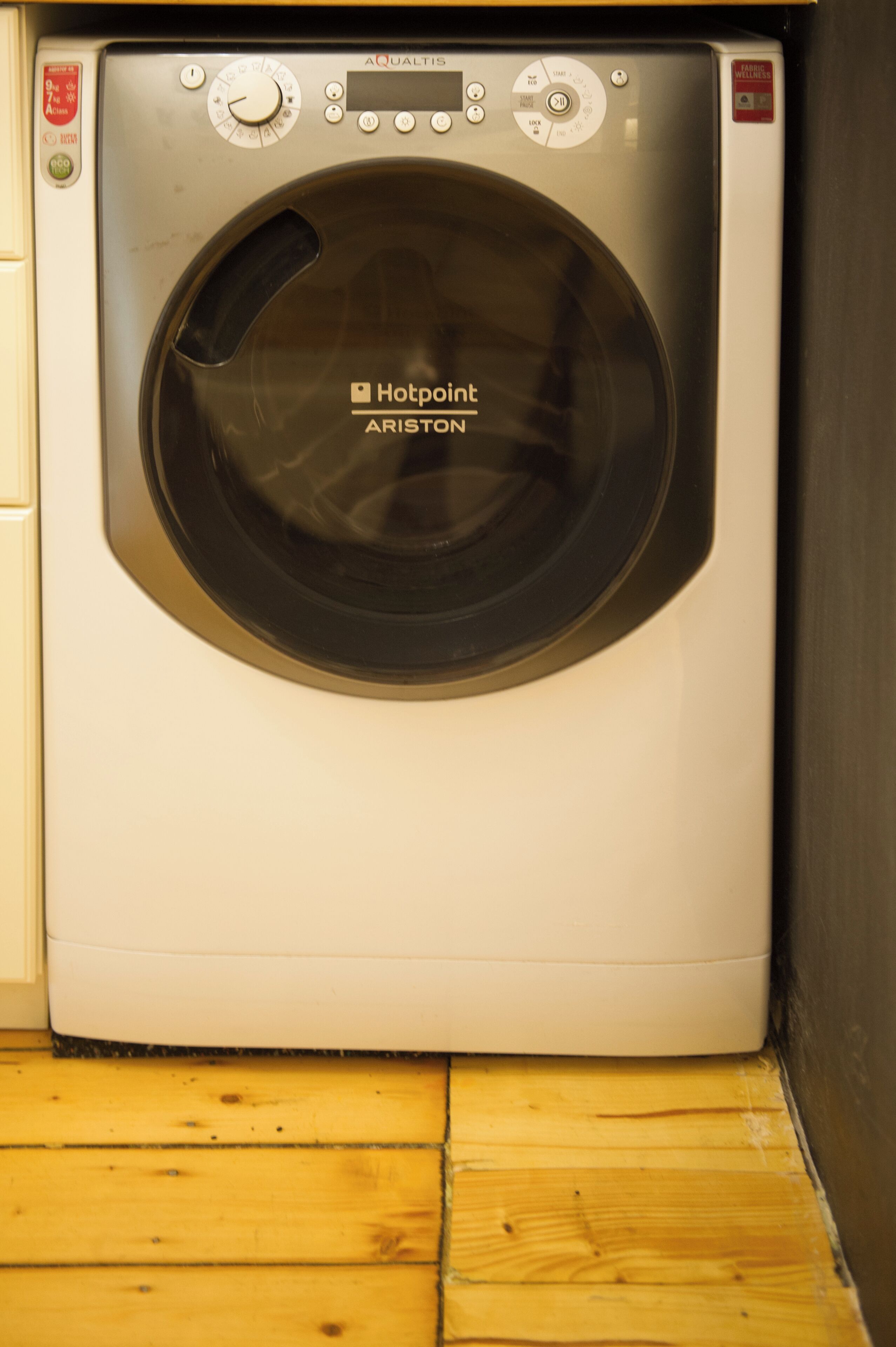 A front view of a Hotpoint Aries washing machine in a laundry room with wooden flooring.