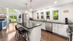 A modern kitchen with a central island, stainless steel appliances, and a coffee sign on the wall. - Juniper Presents: Oasis in the Woods - Hot Tub, Pool & Pizza Oven (New Buffalo)