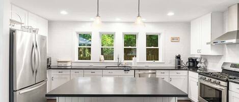 A modern kitchen with a large island, stainless steel appliances, and pendant lighting.