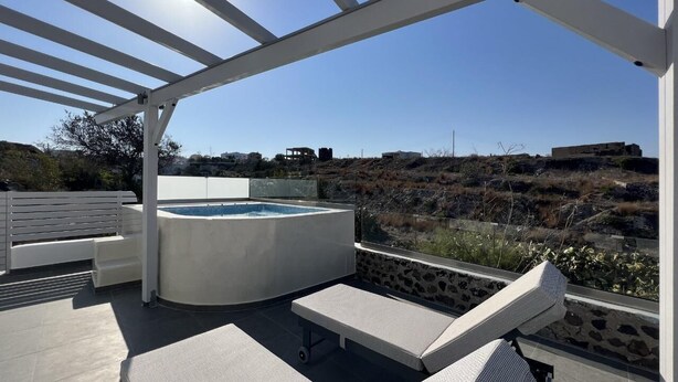A rooftop patio with a hot tub, lounge chairs, and a pergola. - New Villa Sostis (Santorini)