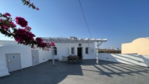 A rooftop patio with a pergola, a table with chairs, and a view of a white building with a blue dome in the background. - New Villa Sostis (Santorini)