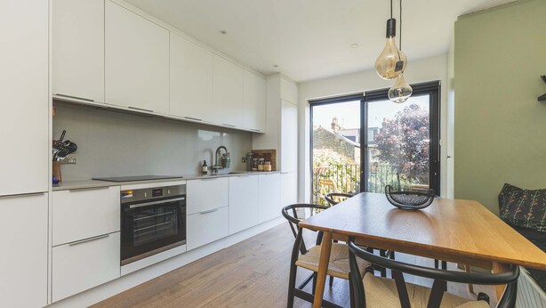 A modern kitchen with white cabinetry, a wooden dining table, and a large window with a view of the outside. - High-End 2BR/2BA with Private Outdoor Space (Greater London)