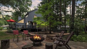Un patio moderno al aire libre con una chimenea, asientos y una terraza con vistas a una zona boscosa.