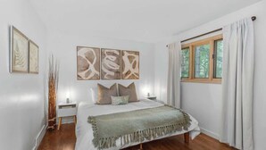 Un dormitorio con cama, mesitas de noche, una ventana con cortinas y decoración en la pared.