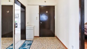 A hallway with two dark wooden doors, a small white cabinet, and a patterned rug on a speckled floor. - Cozy Miranese Venice (Chirignago-Zelarino)