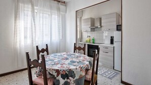 A dining area with a table set for four, a kitchen with white cabinets and appliances, and a window with sheer curtains. - Cozy Miranese Venice (Chirignago-Zelarino)