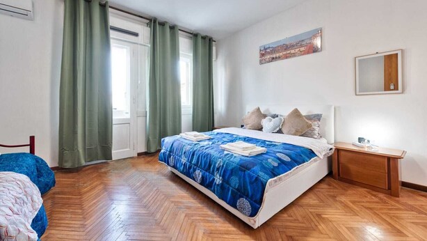 A bedroom with a large bed, wooden flooring, a nightstand, a mirror, and a window with curtains. - Cozy Miranese Venice (Chirignago-Zelarino)