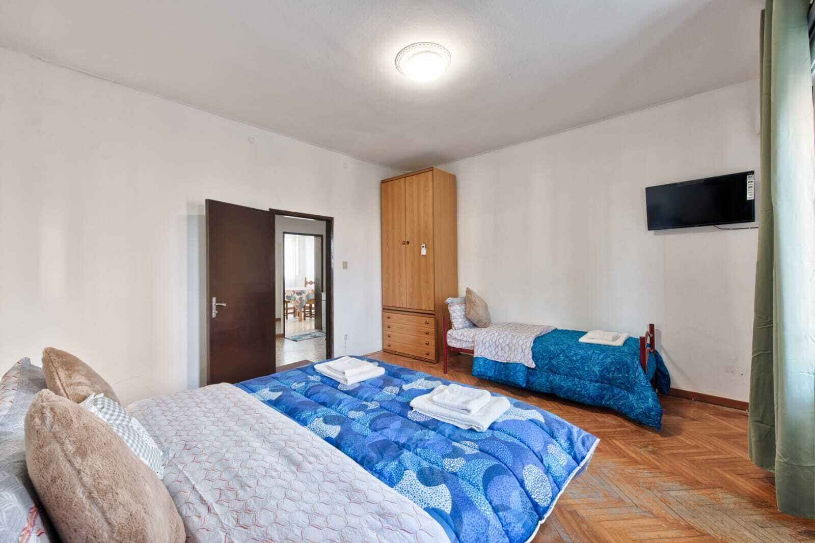 A bedroom with two beds, a wardrobe, a television, and a door leading to another room.