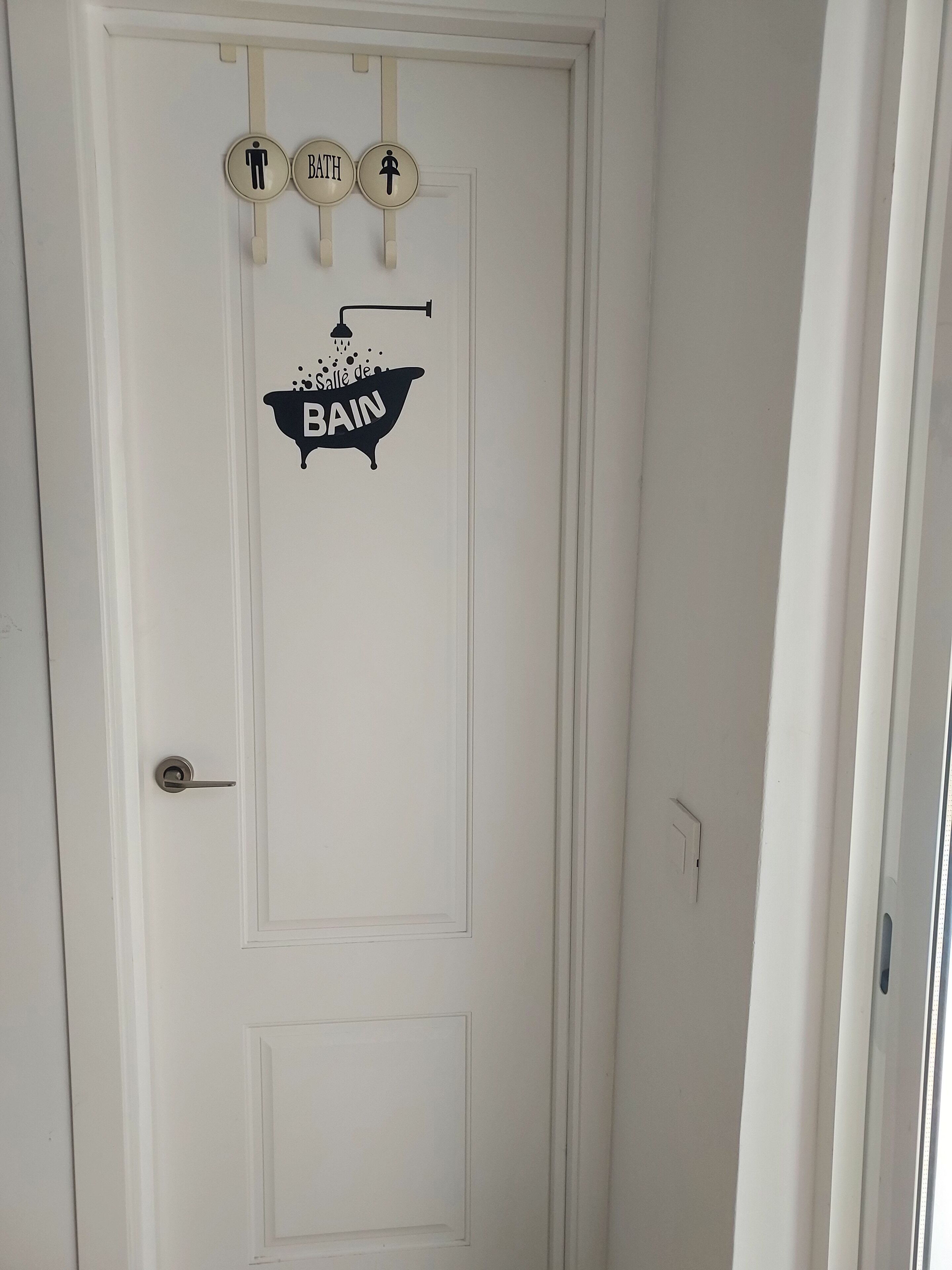 A white door with a bathroom sign and two toilet signs above it.