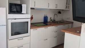 Eine kleine Küche mit weißen Schränken, einer Mikrowelle, einem Backofen, einer Spüle und einem Fernseher.