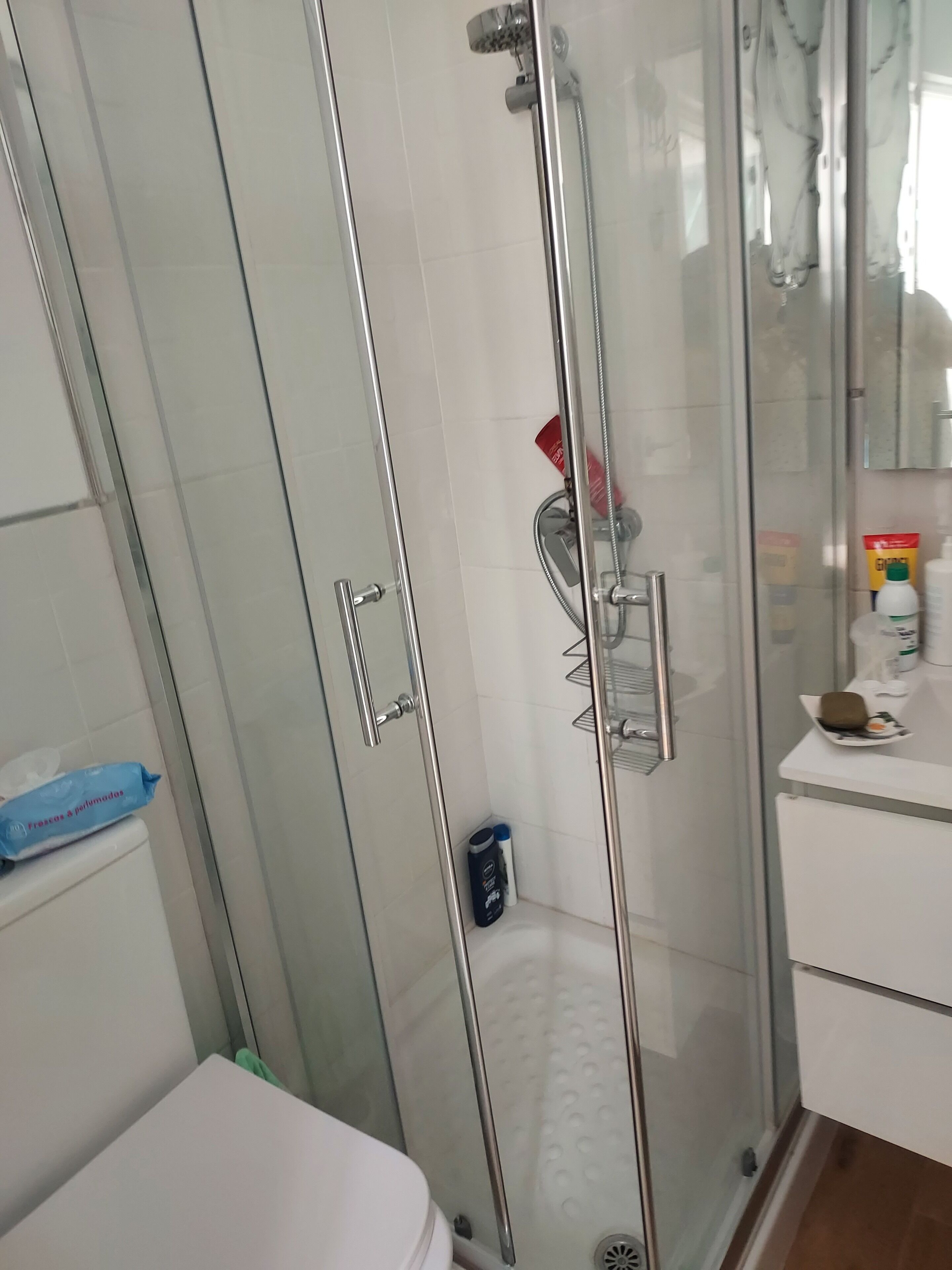 Eine Duschkabine mit Glaswänden, einer Handbrause, einer Glastür und einer weiß gefliesten Wand.