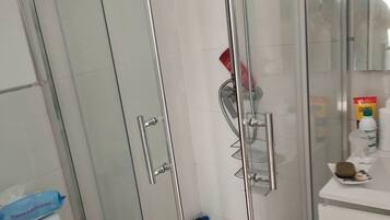 Eine Duschkabine mit Glaswänden, einer Handbrause, einer Glastür und einer weiß gefliesten Wand.