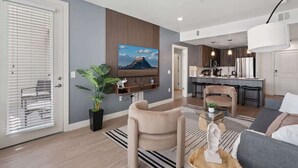 Ein modernes Wohnzimmer mit einer Couch, einem Couchtisch und einem Essbereich, im Hintergrund ist eine Küche zu sehen.