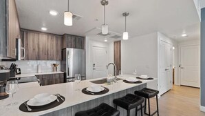 A modern kitchen with a large island, bar stools, and pendant lighting.
