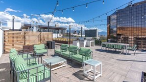 An outdoor seating area with green-striped furniture, a barbecue grill, and string lights.