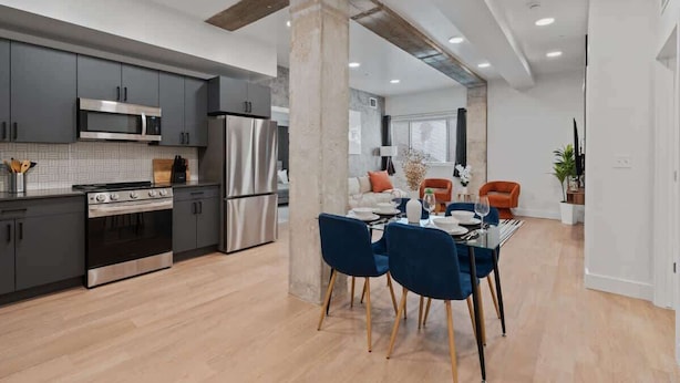 A modern kitchen with grey cabinets, stainless steel appliances, and a dining area with blue chairs and a table.