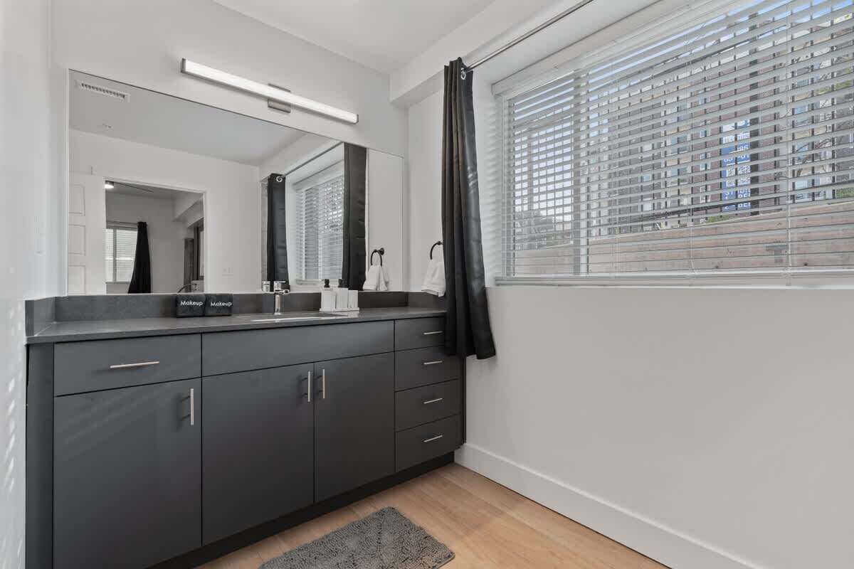 A modern bathroom with dark cabinetry, a large mirror, and a window with blinds.
