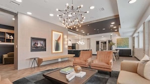 A modern living room with a fireplace, leather armchairs, a coffee table, and a large chandelier.