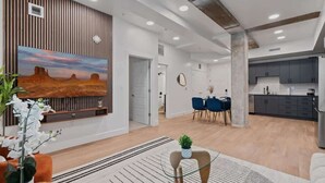 A modern living room with a wooden accent wall, a large painting, and a dining area with blue chairs.