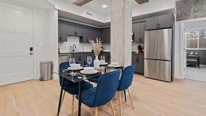 A modern kitchen with grey cabinets, a stainless steel refrigerator, and a dining area with a glass table and blue chairs.