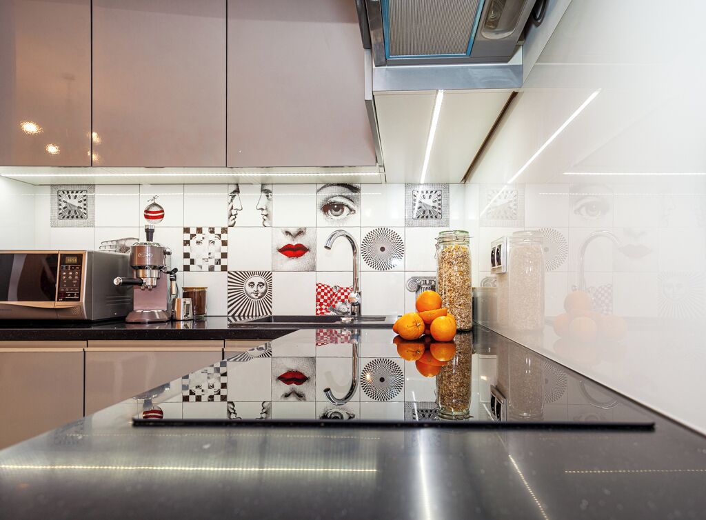 Una cucina moderna con un piano di lavoro nero, elettrodomestici in acciaio inossidabile e un rivestimento decorativo con diversi motivi e immagini.
